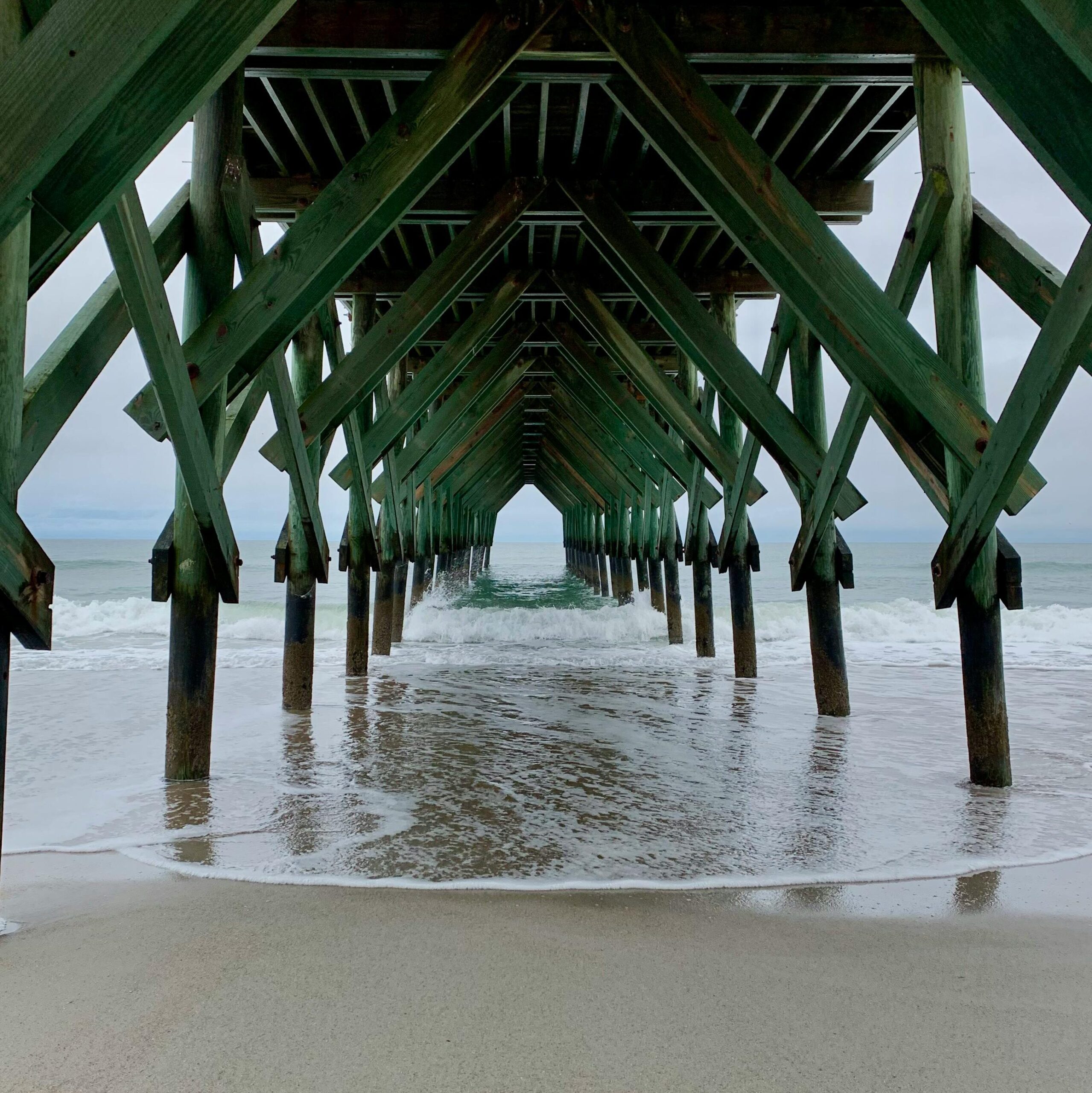 Waves crash under the green wooden pier at Wrightsville Beach, NC.